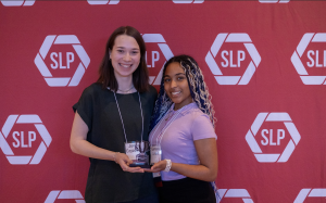 Two woman holding an award smiling in front of a red backdrop.